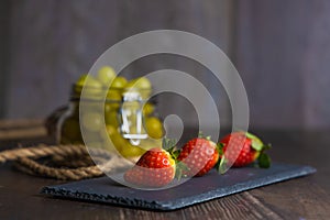 Bodegon fruit, fresh strawberries on slate plate with glass jar with fresh grapes on aged basis