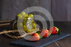 Bodegon fruit, fresh strawberries on slate plate with glass jar with fresh grapes on aged basis