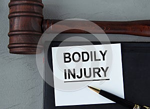 BODILY INJURY - words on a white sheet with leather notebooks, a judge\'s hammer and a pen