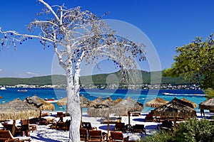 Bodrum, Turkey - August 2020: Lujo`s snow white beach with baboon umbrellas, wooden sunbeds, emerald colored Aegean Sea photo