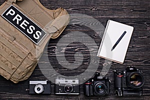 Body armor, camera, notebook and pen on wooden background