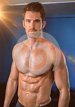 Body builder with flare against a blue wall