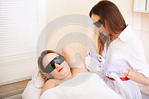 Body Care. Beautiful girl lies in the office of a beautician in goggles from laser irradiation, the hands of the doctor