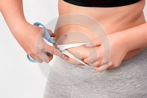 Body Care. Chubby girl with bare belly standing isolated on white cutting fat with scissors close-up