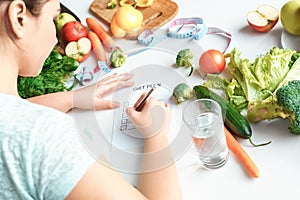 Body Care. Chubby girl sitting at kitchen table with glass of water writing diet plan concentrated close-up