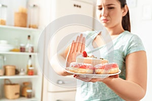 Body Care. Chubby girl standing in kitchen holding plate with desserts reject temptation close-up blurred background