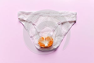 Body care gynecology and woman`s health. Woman panties and half of tangerine fruit in an intimate part