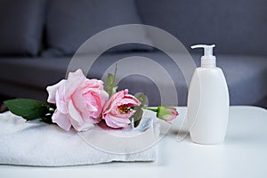 Body care product white bottle with shower gel or shampoo and towel with pink flowers rose. Bath preparation. room interior