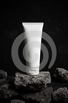 Body cream lotion bottle luxury packaging tube with stone rock concrete grunge on dark black background, aroma spa smell treatment