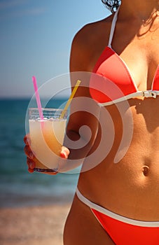 Body of girl in swimsuit. She holds glass of juice