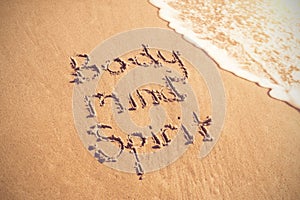 Body mind spirit text written on sand with surf
