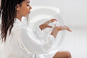 Body Nourishing. Beautiful African American Woman Applying Moisturising Lotion On Hand