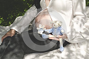 Body part Pregnant belly and hand holding baby toy teddy bear