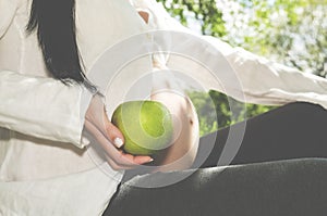 Body part Pregnant belly and hand holding green apple