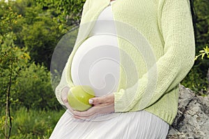 Body part Pregnant belly and hand holding green apple with white dress