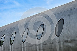 The body of the plane with circular windows shows a silver metallic surface of an idle airplane on the sky background