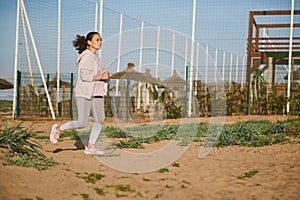 Body positive woman in activewear, running on the beach, burning calories, jogging on the sand. Sport. Endurance. People