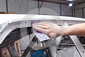 The body repairman grinds the white car`s frame with purple emery paper in preparation for painting after applying putty in a