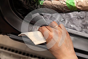 The body repairman grinds the white car`s frame with purple emery paper in preparation for painting after applying putty in a photo