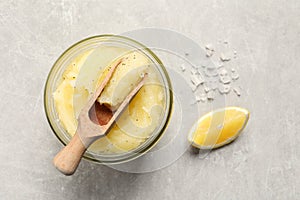 Body scrub with scoop, sea salt and lemon on light grey table, flat lay