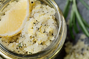 Body scrub of sea salt with lemon, rosemary and olive oil in glass jar on stone table