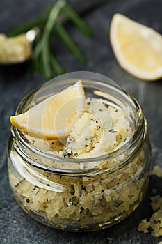 Body scrub of sea salt with lemon, rosemary and olive oil in glass jar on stone table