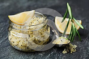 Body scrub of sea salt with lemon, rosemary and olive oil in glass jar on stone table
