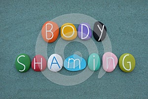 Body shaming, creative composition with multicolored stone letters over greensand