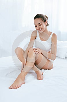 Body Skin Care. Beautiful Woman Touching Long Legs On White Bed