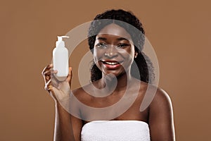 Body Skin Moisturising. Attractive Black Female In Towel Holding Bottle With Lotion