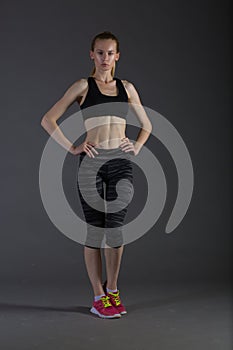 Body of slim female in activewear doing posin on gray low key, perfect blonde