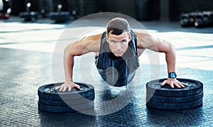 The body will do what the mind tells it. a young man doing push ups with weights in a gym.