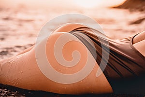 Body of woman in black swimwear relaxing at sea with sunset colors.