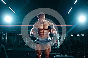 Bodybuilder athlete man pumping up muscles in the gym with dumbbells. Brutal strong muscular guy on fitness workout