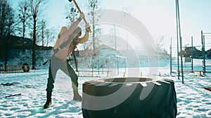 Bodybuilder with a ballon compressed air drager on his back and in a full face mask hits a big tire with a sledgehammer