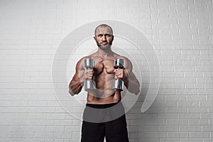 Bodybuilder doing exercises for biceps with a dumbbells against brick wall