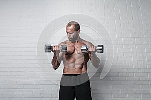 Bodybuilder doing exercises for biceps with a dumbbells against brick wall