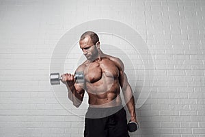 Bodybuilder doing exercises for biceps with a dumbbells against brick wall