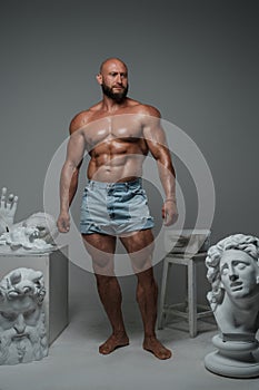 Bodybuilder dressed only in shorts posing around greek statues