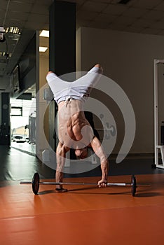 Bodybuilder Exercising Handstand Push-Ups On Barbell In Gym