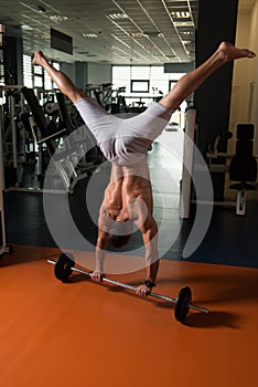 Bodybuilder Exercising Handstand Push-Ups On Barbell In Gym