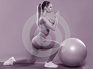 bodybuilder girl in a lilac tracksuit, sitting on a mat with a Pilates ball, cardio workout. Sports concept,