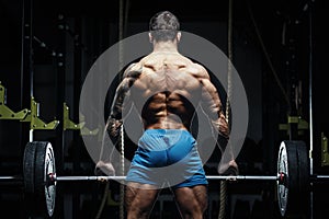 Bodybuilder with great physique and body shape training with barbell in gym over dramatic light