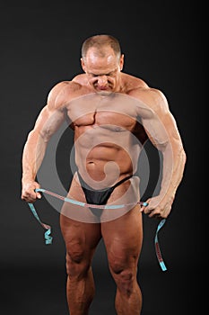 Bodybuilder holds measuring tape and looks down