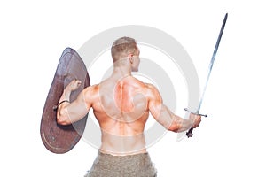 Bodybuilder man posing with a sword and shield isolated on white background. Serious shirtless man demonstrating his