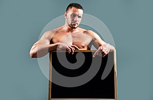 Bodybuilder man with sign advertising board. Strong athlete holding blank poster isolated on gray background. Handsome