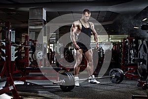 Bodybuilder man standing with barbell, workout in gym