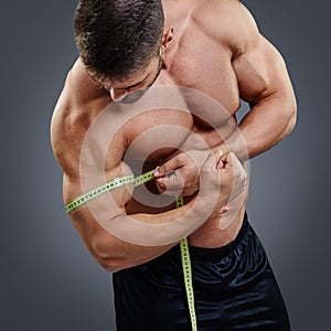 Bodybuilder measuring biceps with tape measure