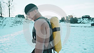 Bodybuilder with a naked torso stands against the backdrop of the sun in a winter park with a ballon compressed air