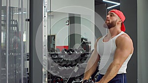 Bodybuilder performs exercise in biceps simulator in the gym. Sports training